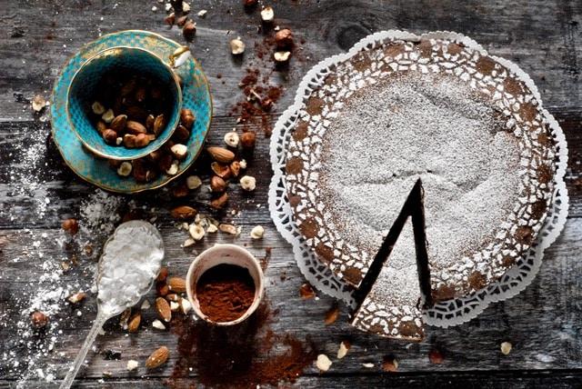 Overhead view of a Torta Di Caprese dusted with confectioners sugar, placed on a rustic wooden background with scattered ingredients around.