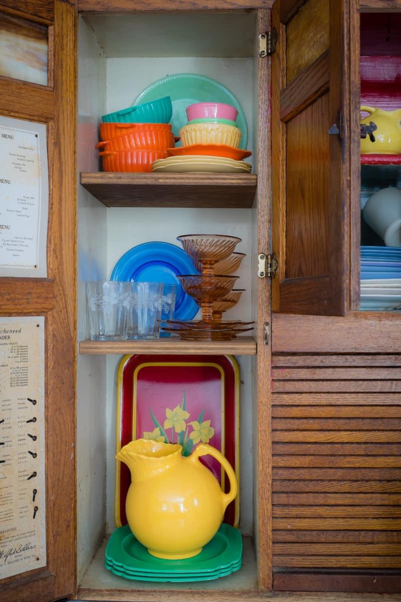 A vintage wooden hoosier cabinet with colorful dishes