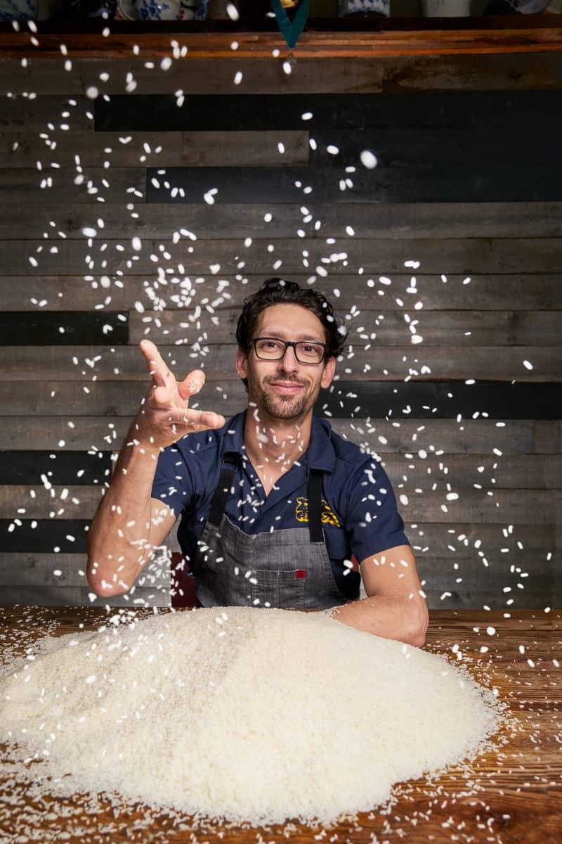 Chef Abraham Conlon animatedly tossing rice into the air, capturing a moment of culinary passion.