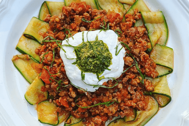 Dish of Zucchini Pappardelle Arrabbiata with a dollop of cream and pesto on top.